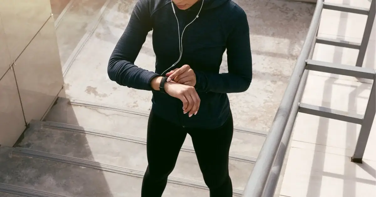 A woman wearing a black tracksuit is checking the time on her watch.